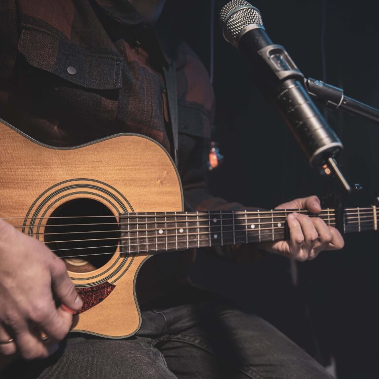 Close up a man plays an acoustic guitar in a dark room